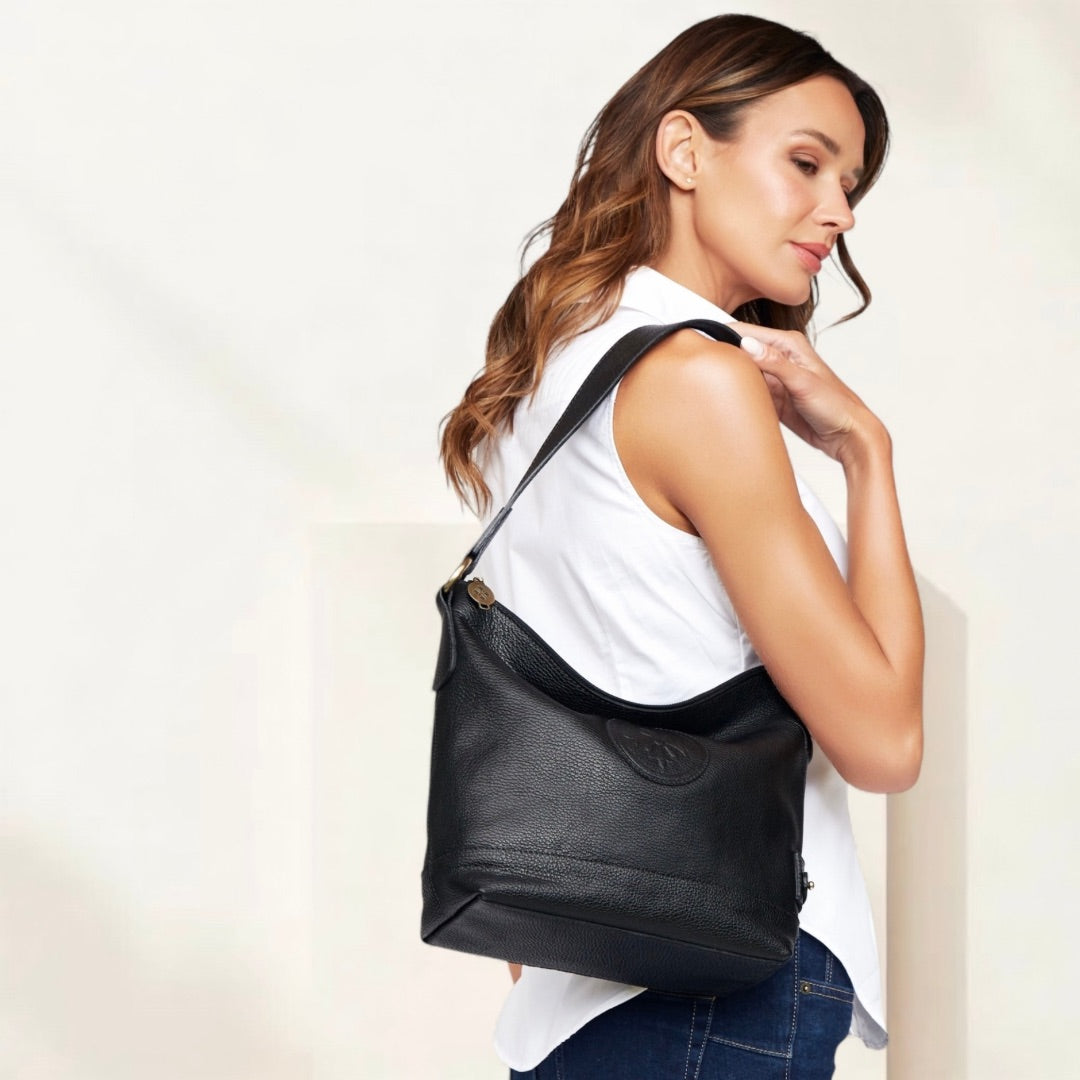 Cartera de hombro SOPHIA de cuero natural negro, al hombro de la modelo, con el logo en relieve